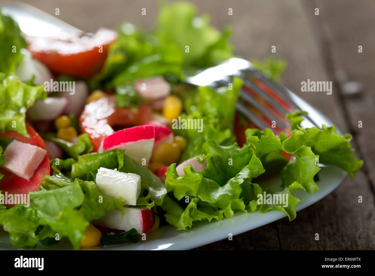 Fresh salad with sweetcorn and cheese in plate over wood background Stock Photo