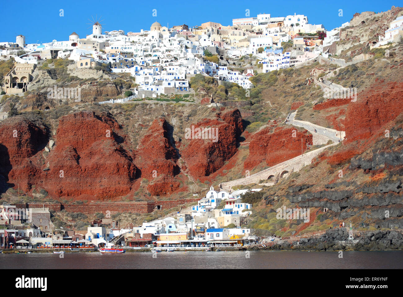 Oia, Santorini, town and red cliffs below with port, Greece Stock Photo