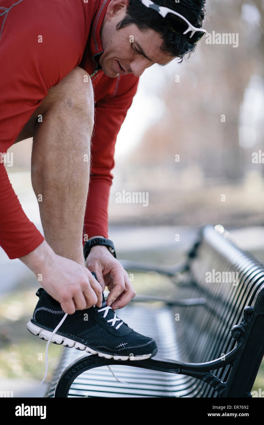 A young man prepares to jog in a park and ties his shoe. Stock Photo