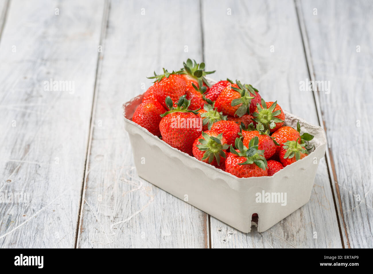 Strawberries in a paper bowl on a wooden table Stock Photo
