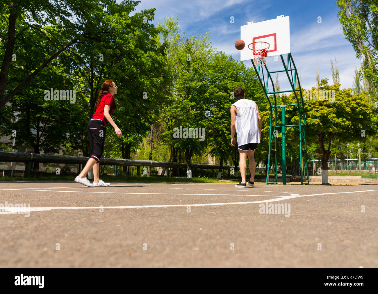 Young Athletic Couple Playing Basketball Together on Outdoor Court in Lush Green Park Stock
