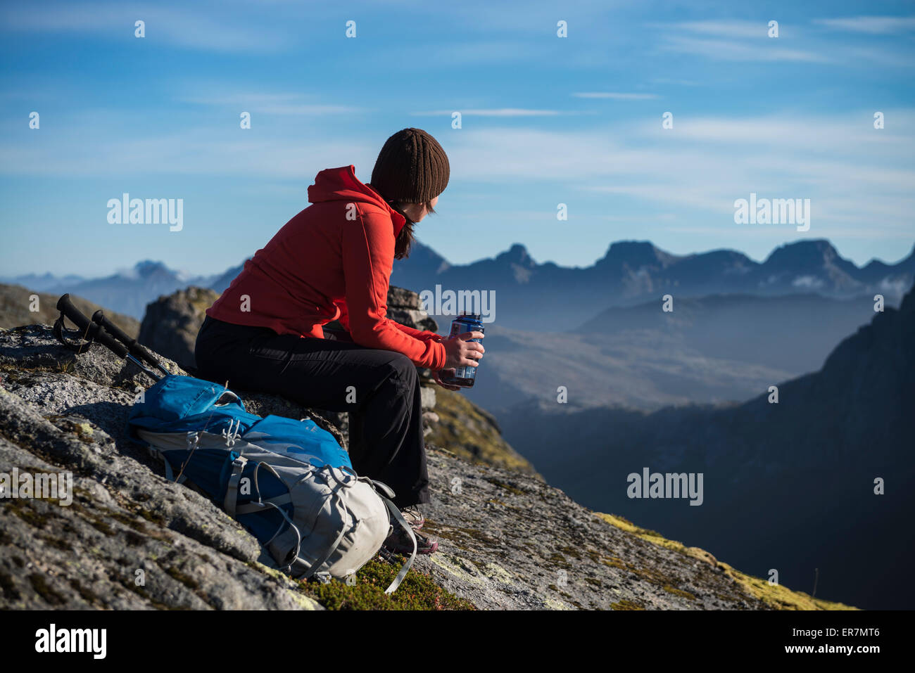 Female hiker takes a break and enjoys mountain views, Moskenesøy, Lofoten Islands, Norway Stock Photo
