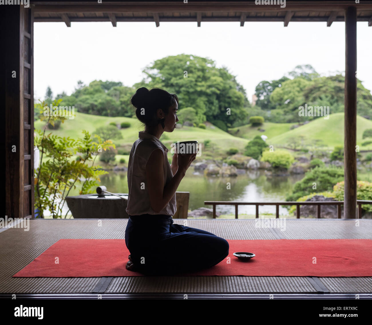 Young Japanese woman drinking green tea at the Kokin-Denju-no-Ma teahouse, Suizenji Jojuen Park, Kumamoto City Stock Photo