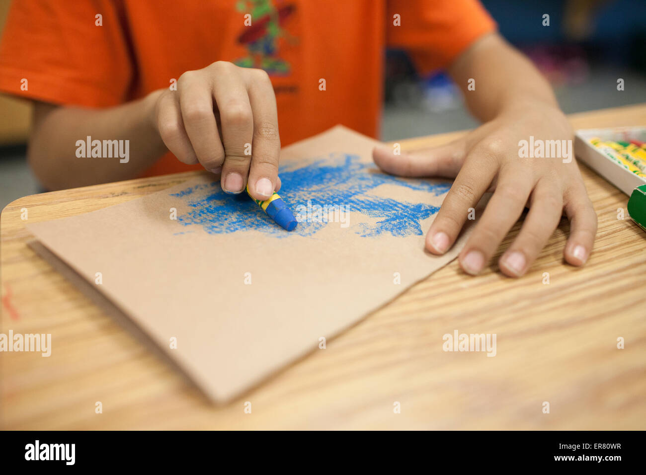 A young boy colors using a blue crayon. Stock Photo