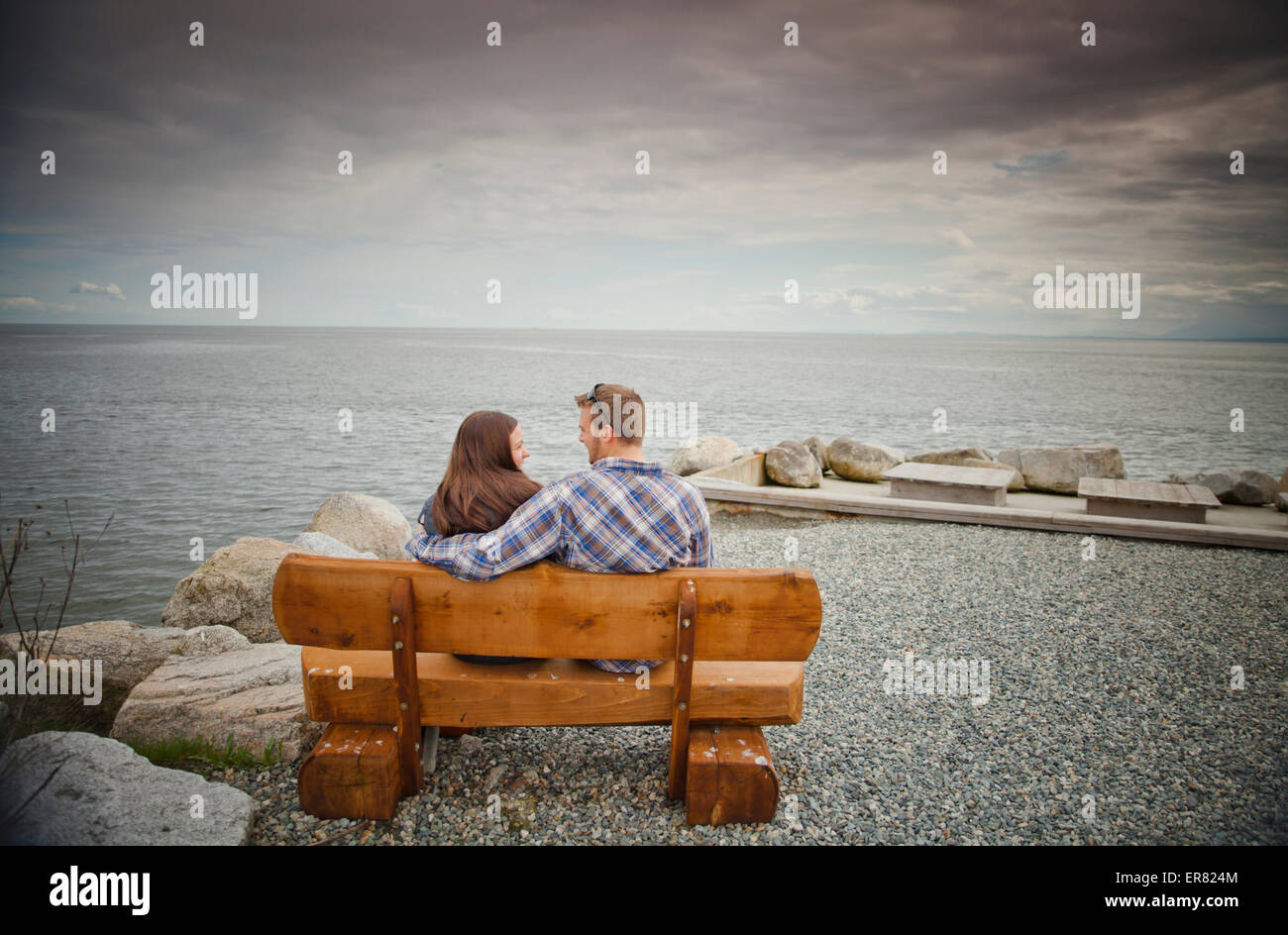 A couple share a laugh while sitting on a log bench. Stock Photo