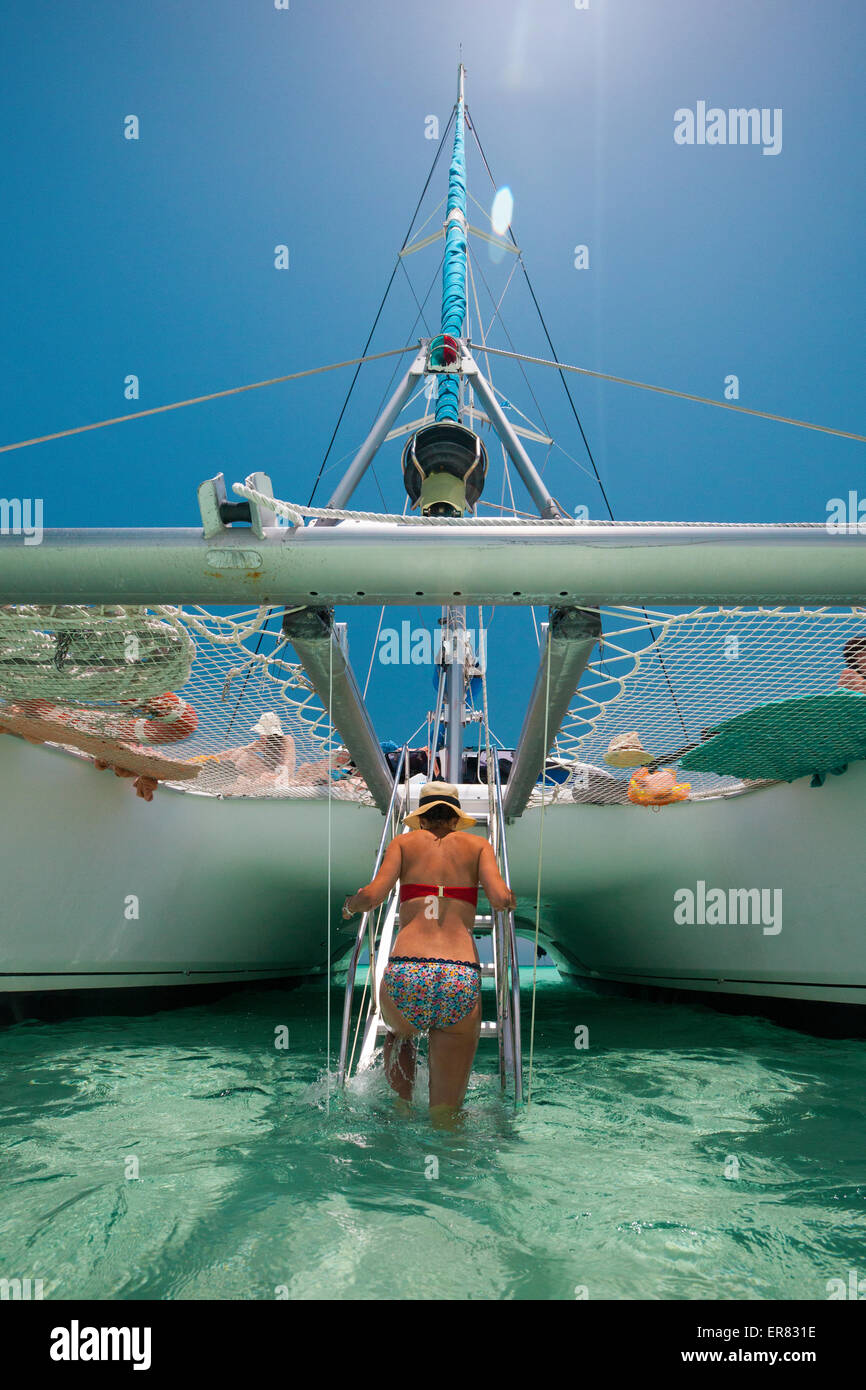 A young woman climbs up ladder to a  catamaran boat after swimming in tropical water. Stock Photo