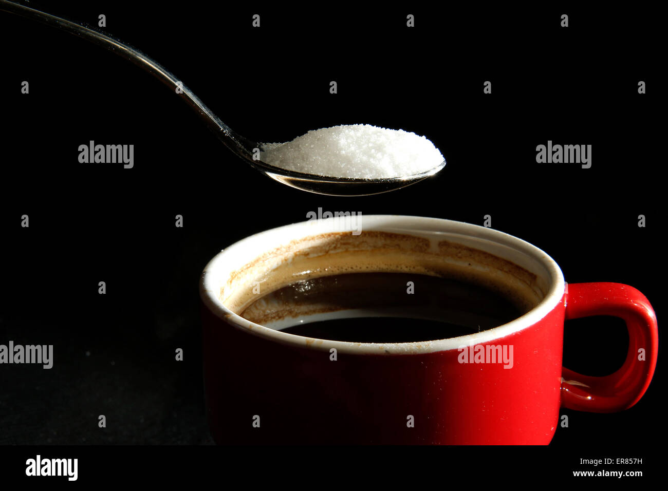 A spoonful of sugar is poured into a cup of coffee Stock Photo