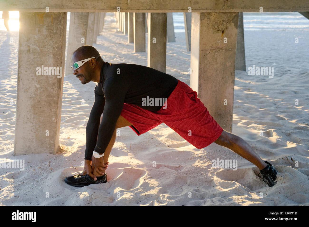A man stretching under a beach pier Stock Photo