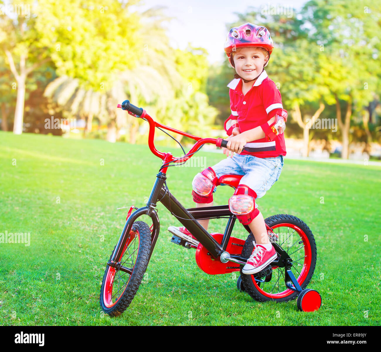Cute little boy riding a bike in the park in bright sunny day, spending leisure time outdoors, enjoying summer sport Stock Photo