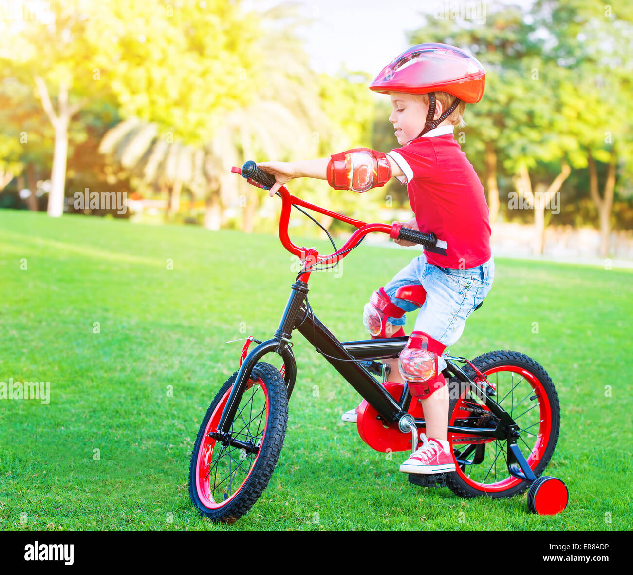Little boy on bicycle wearing red protective helmet, having fun in the park, active childhood, enjoying cycling, summer holidays Stock Photo
