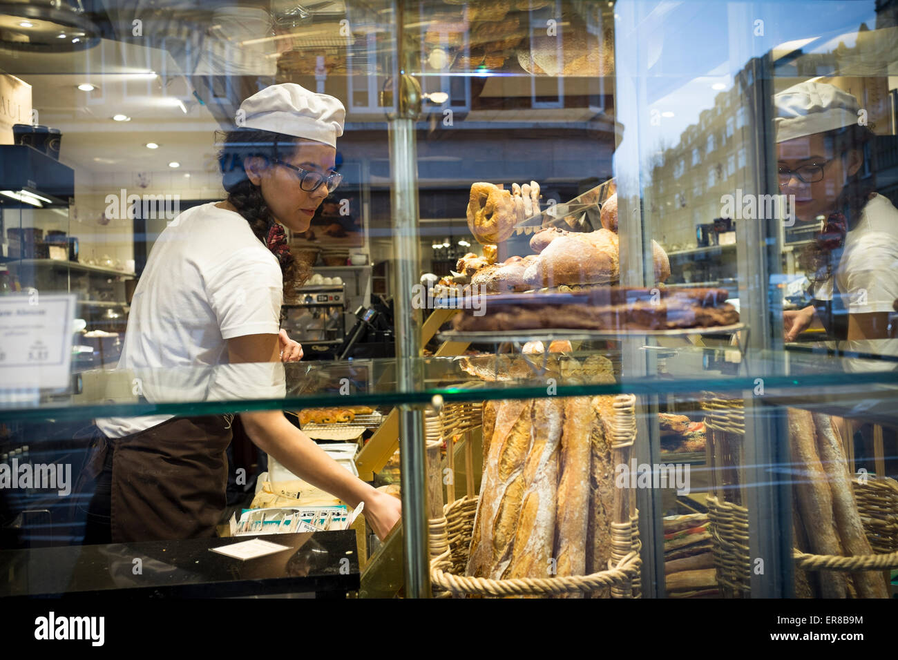 Young female baker seen through bakery window, London, UK Stock Photo