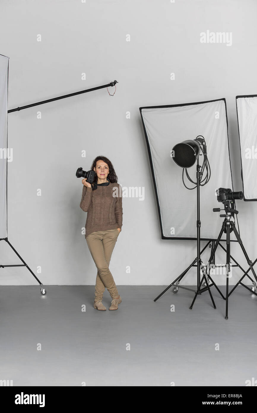 Full length of mature female photographer with camera in photo studio Stock Photo