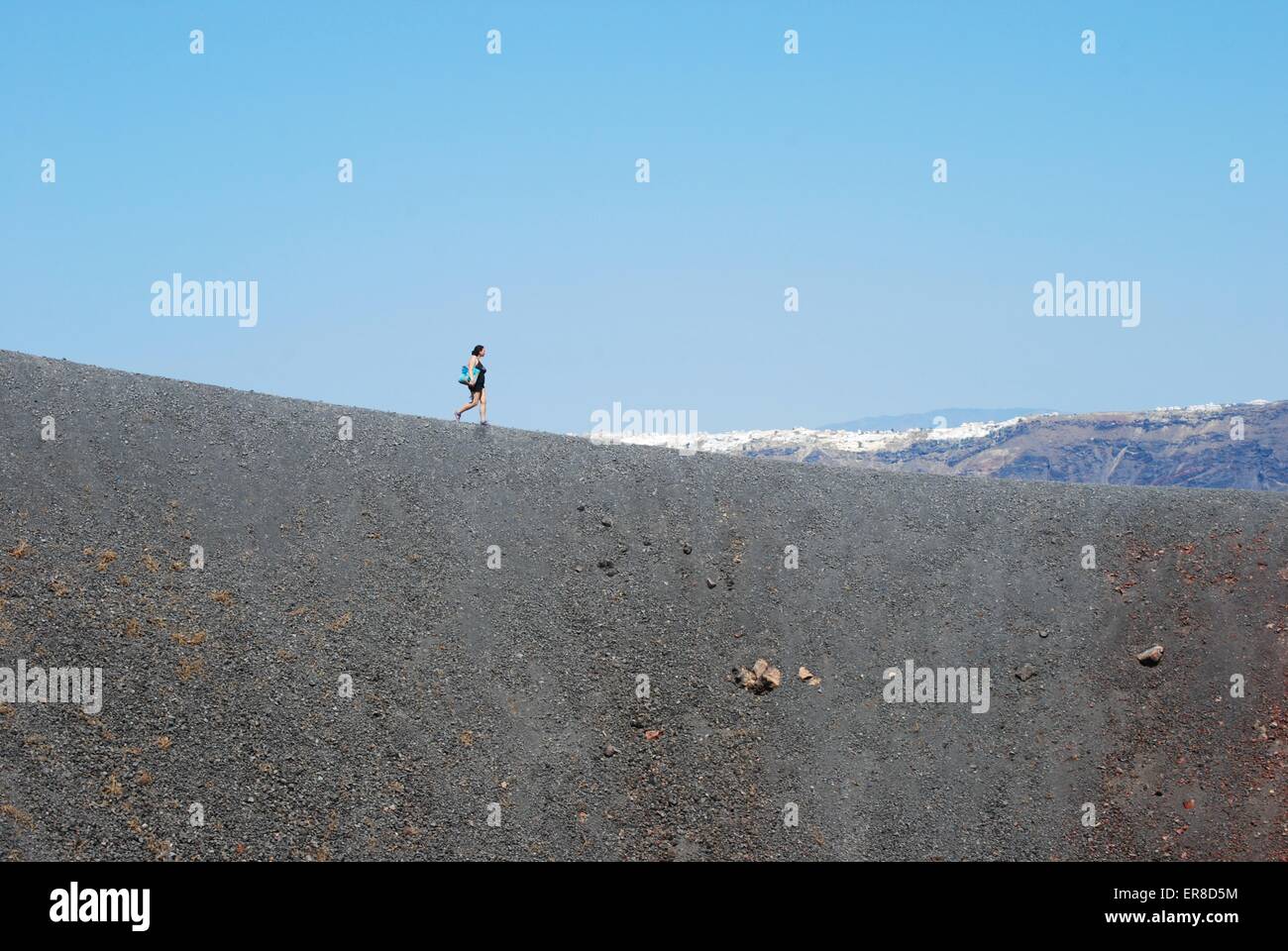 Tourist walking along the crater ridge on the active volcano central island of Santorini, Greece. Stock Photo