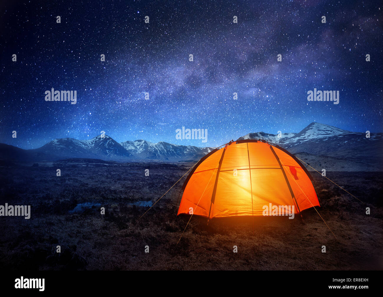 A camping tent glows under a night sky full of stars. Outdoor Camping adventure. Stock Photo
