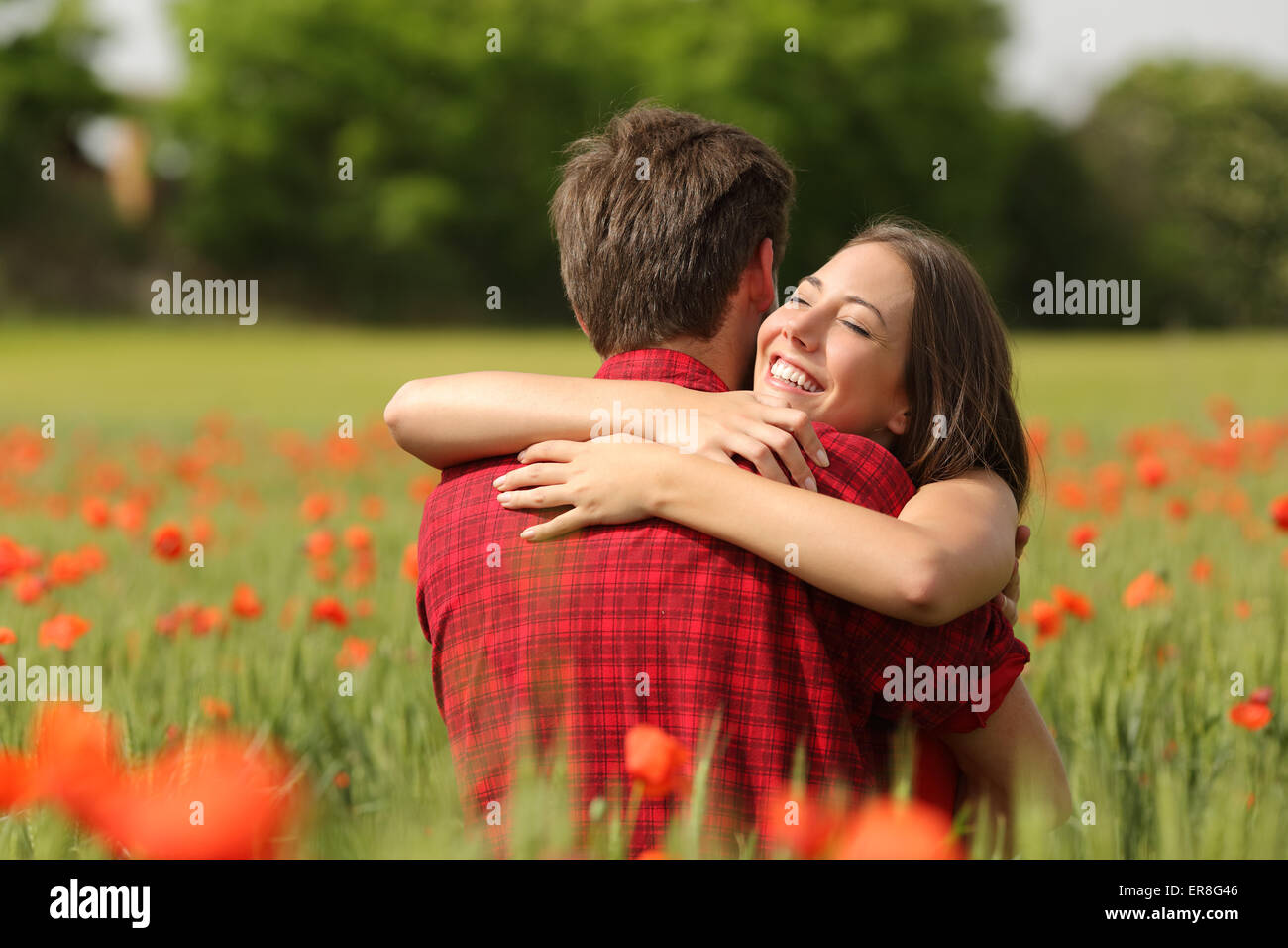 Happy couple hugging affectionate after proposal in a green field with red flowers Stock Photo