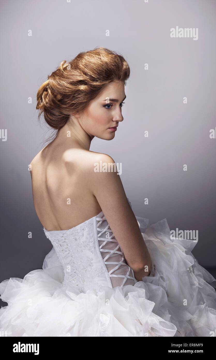 Sad young bride in wedding dress standing against gray background Stock Photo