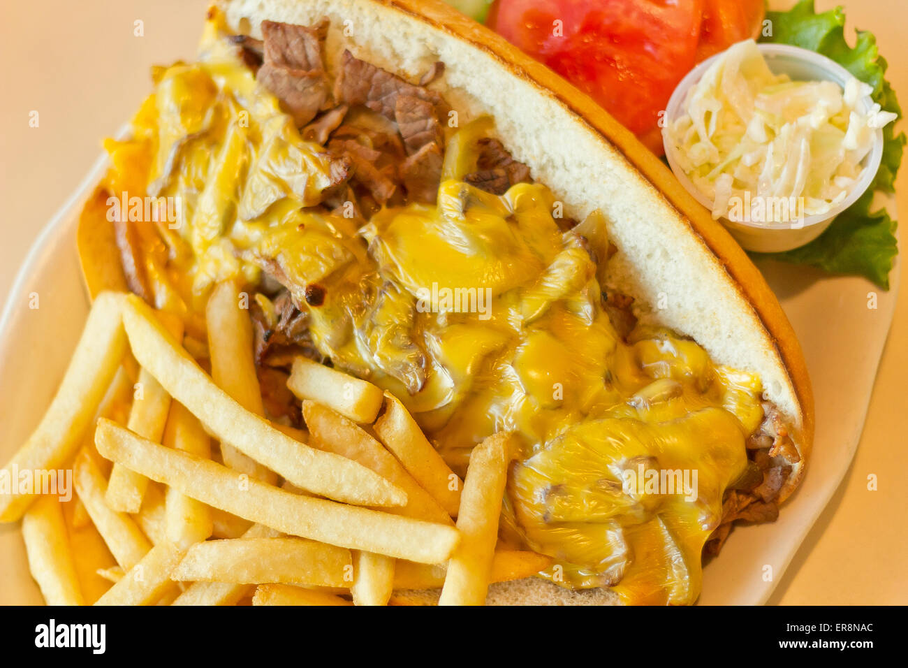 A messy Philly Cheesesteak with onions and peppers with fries on the