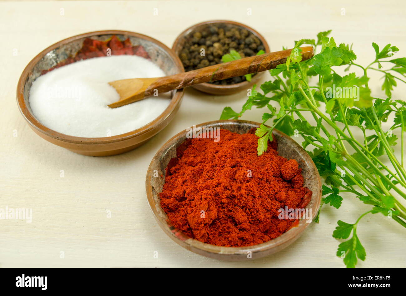 Plates filled with black pepper, paprika and salt and a green herb on a table Stock Photo