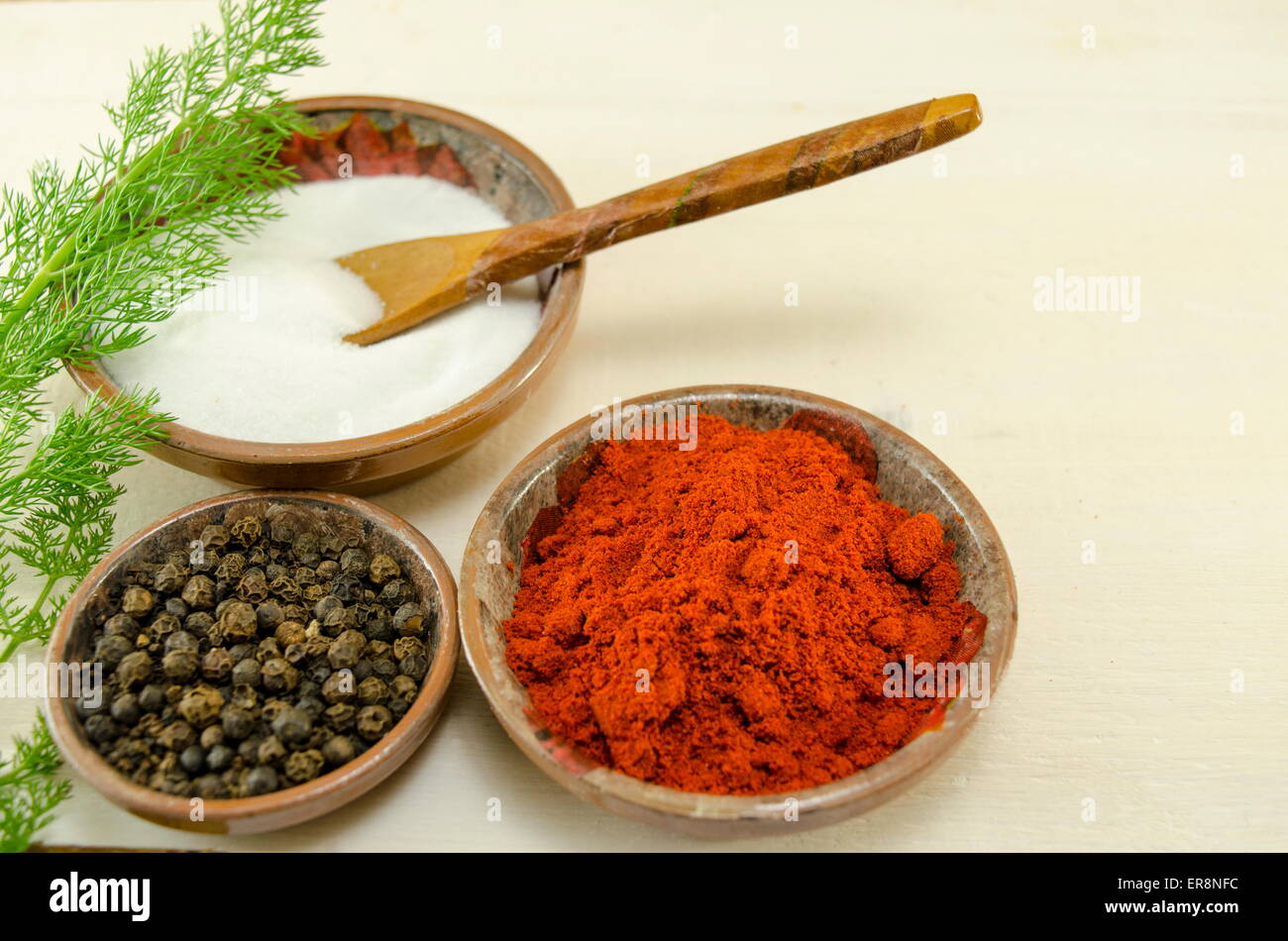 Plates filled with black pepper, paprika and salt and a green herb on a table Stock Photo