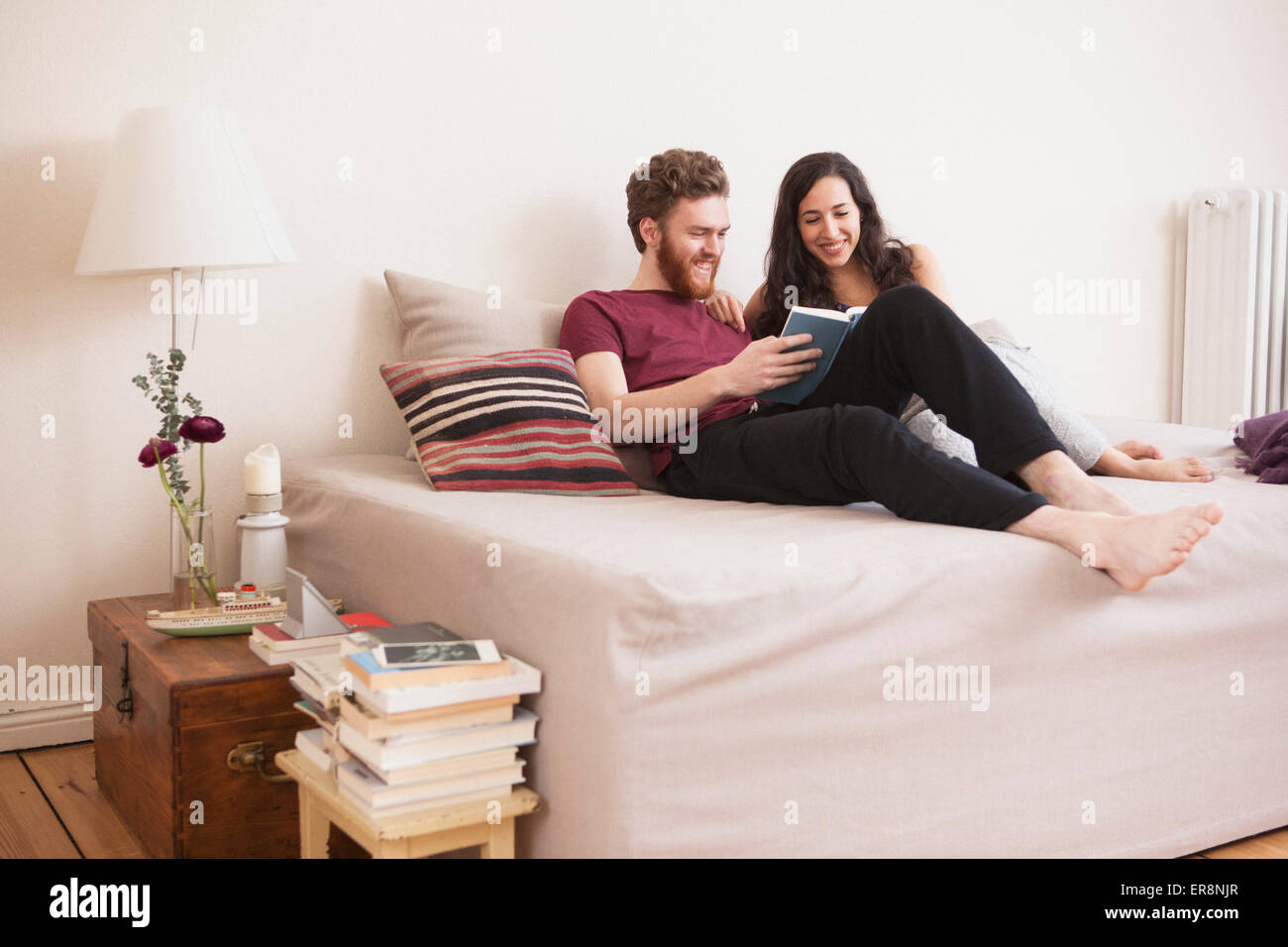 Happy young man reading book for woman in bed Stock Photo
