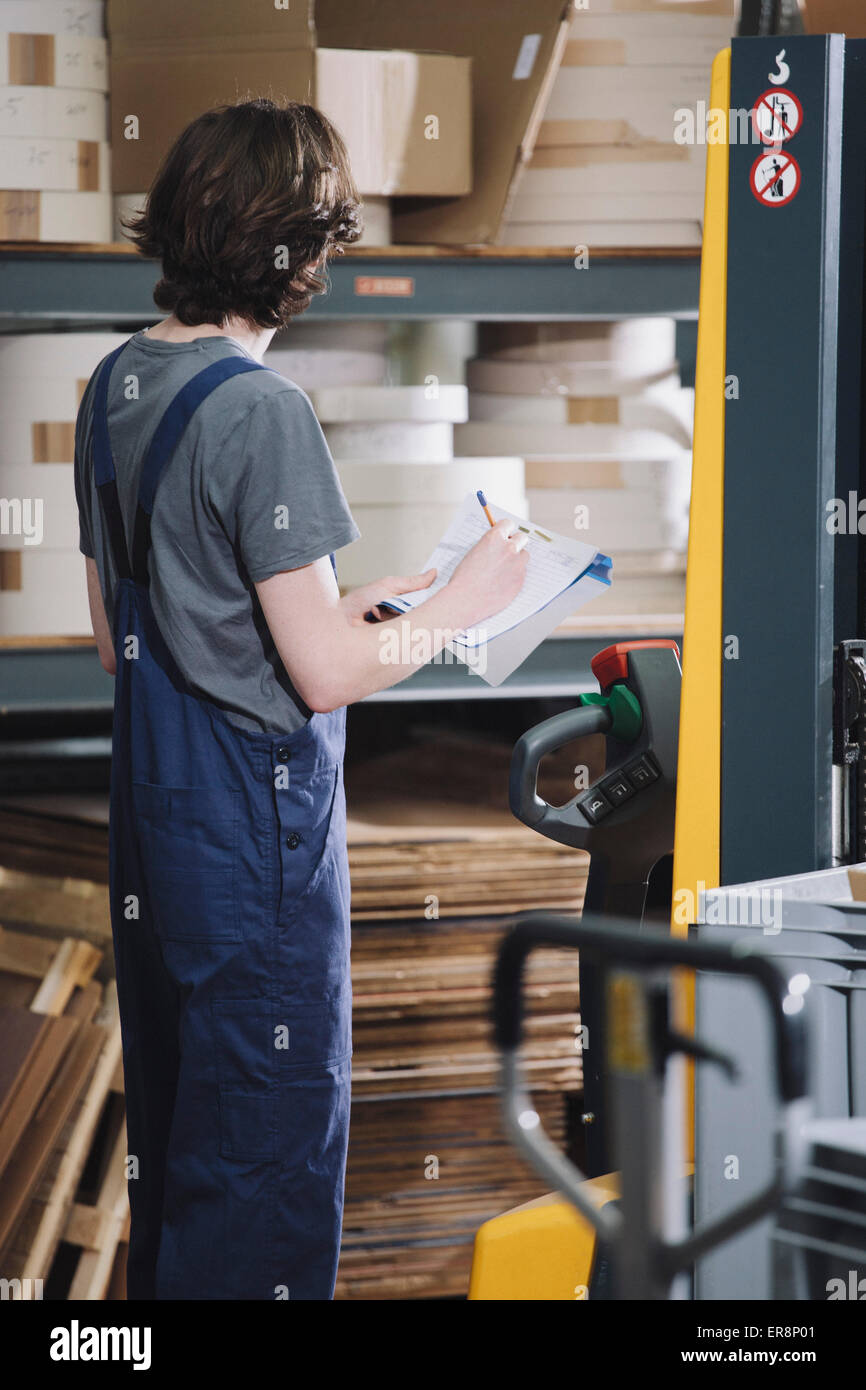 Side view of young manual worker writing on paper in warehouse Stock