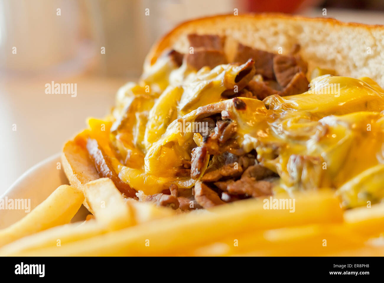 A messy Philly Cheesesteak with onions and peppers with fries on the