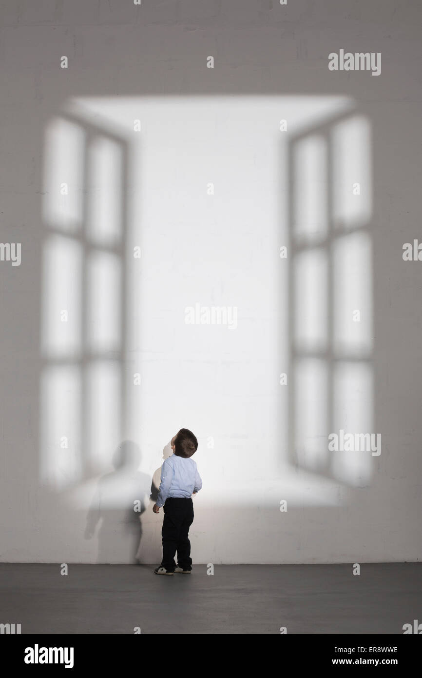 Boy looking at shadow of open window on white wall at home Stock Photo