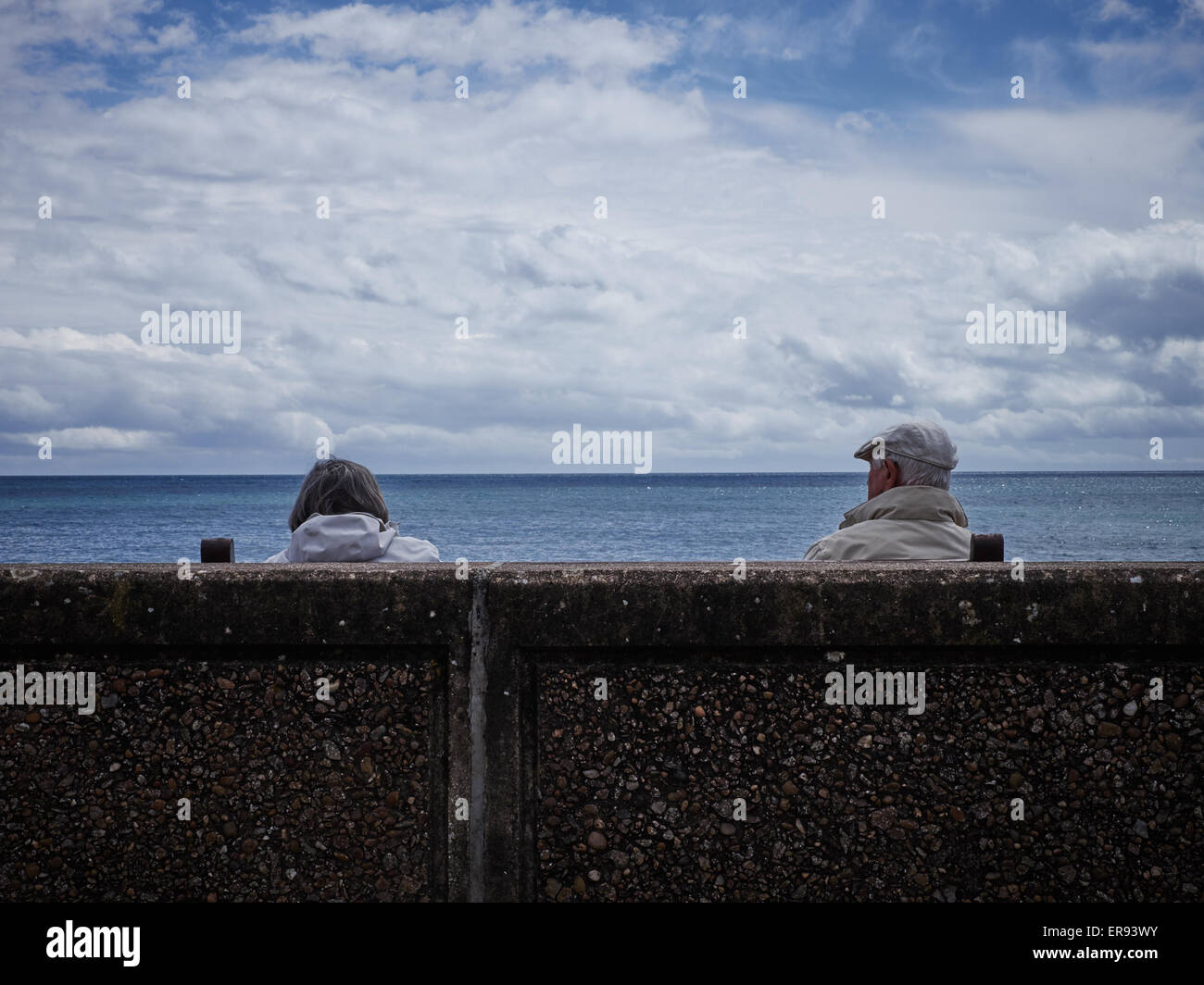 A couple sit behind the sea wall looking out to sea Stock Photo - Alamy