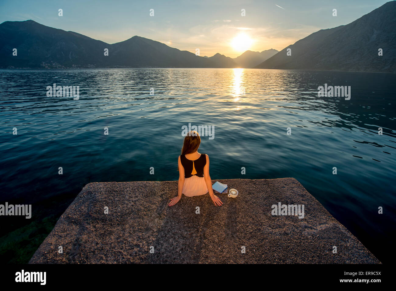 Woman sitting on the pier at sunrise Stock Photo