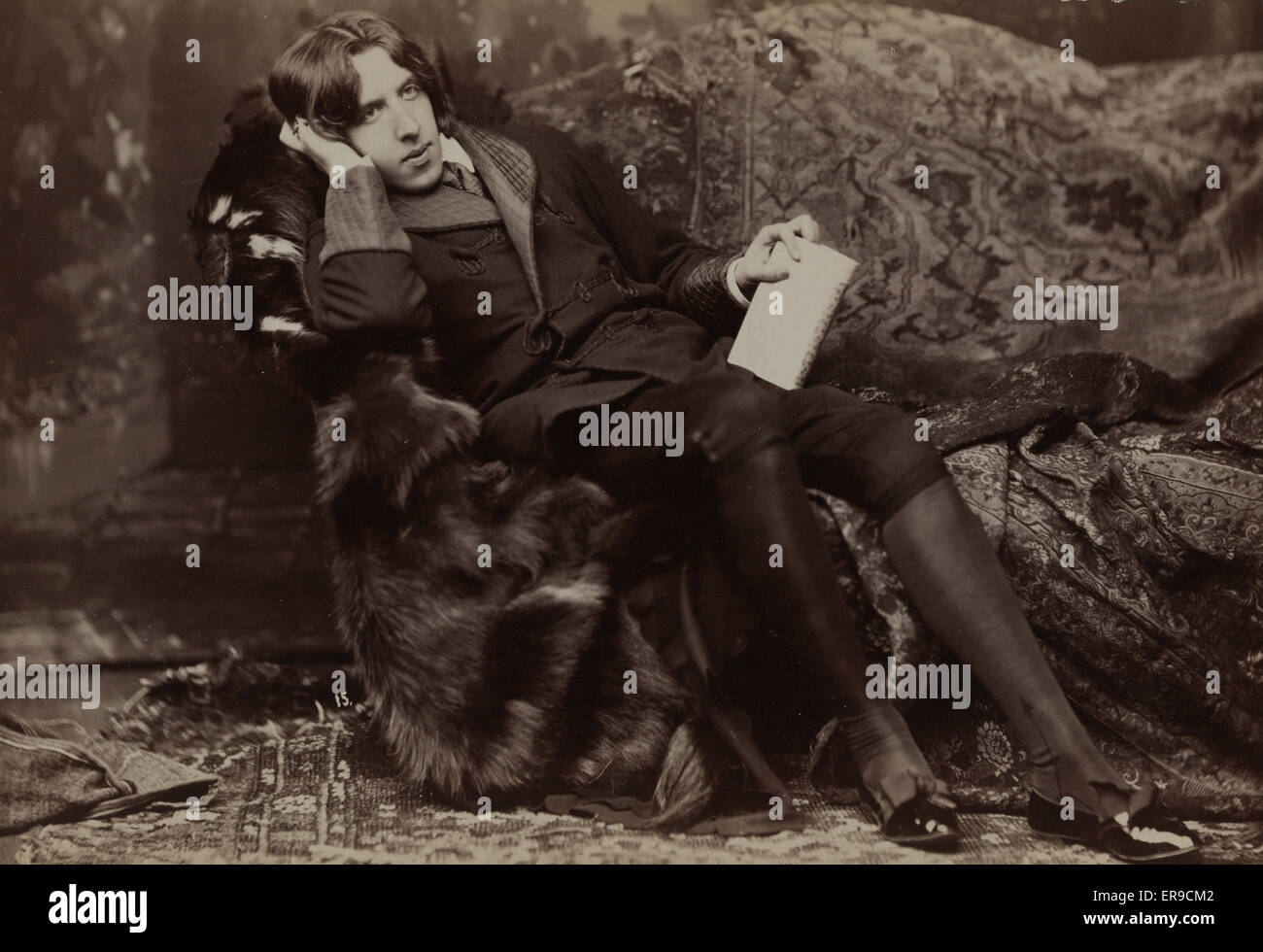 Oscar Wilde. Oscar Wilde, full-length portrait, facing right, sitting in chair, right hand on cheek, left hand holding book. Date c1882. Stock Photo