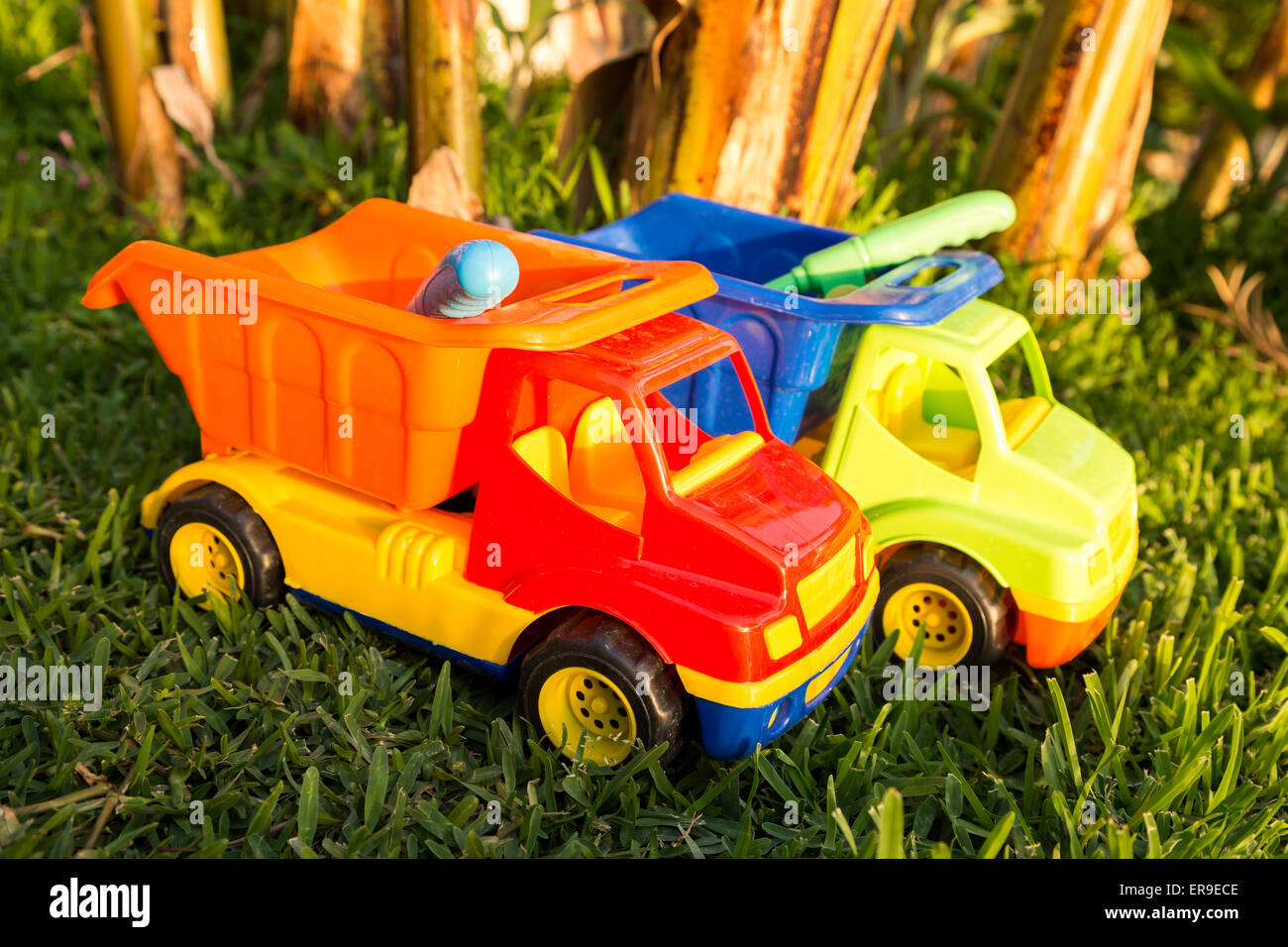 Colorful plastic toy trucks in the grass to symbolize construction and carrying trade business Stock Photo