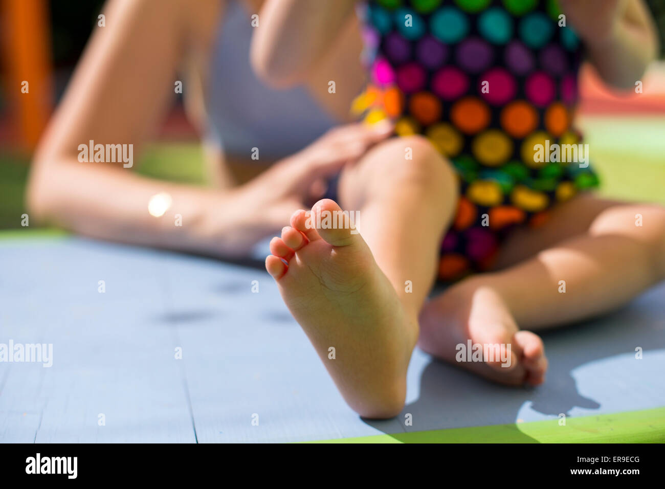 Mother holding her little daughter feet wearing colorful swimsuits on the table closeup Stock Photo