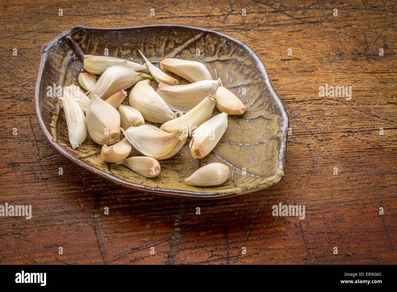 garlic cloves on a ceramic leaf shaped bowl against rustic wood Stock ...