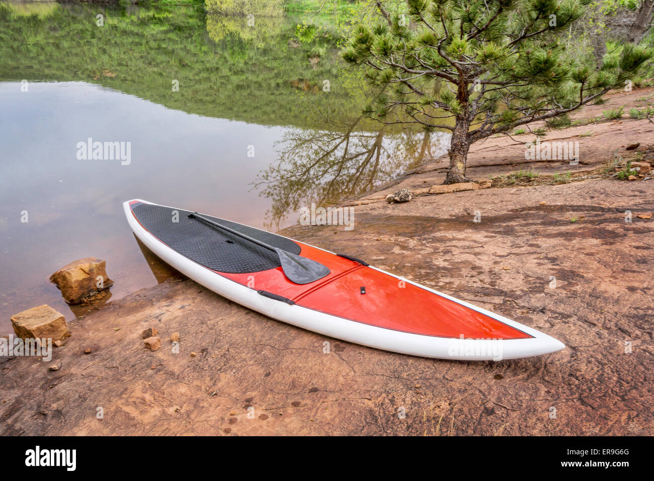 red stand up paddleboard with a paddle on rocky lake shore old