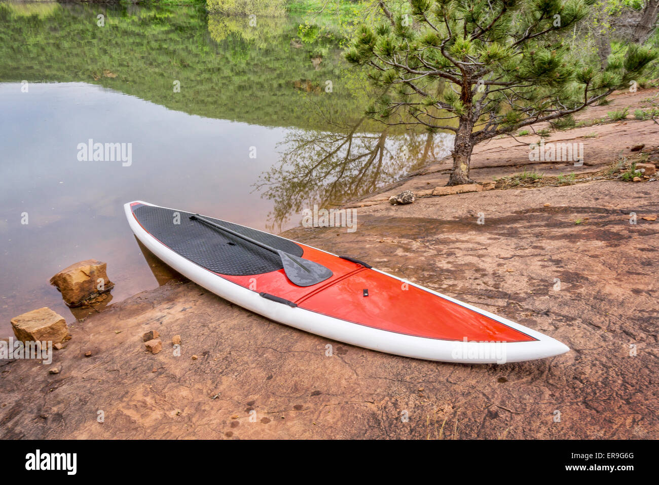 red stand up paddleboard  with a paddle on rocky lake shore - old sandstone quarry at Horsetooth Reservoir Stock Photo