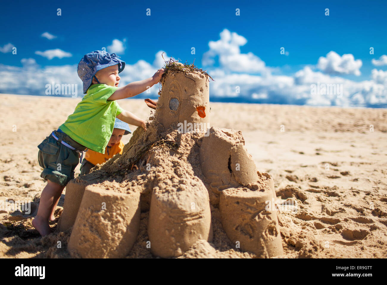 Two little boys in colorful t-shirts building large sandcastle on the beach Stock Photo