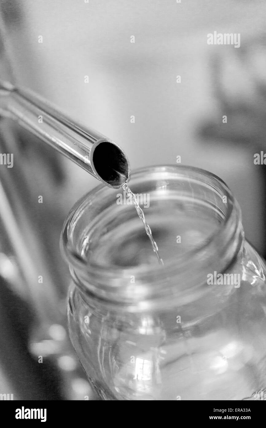 Alcohol pouring into test jar at craft distillery. Vertical B/W