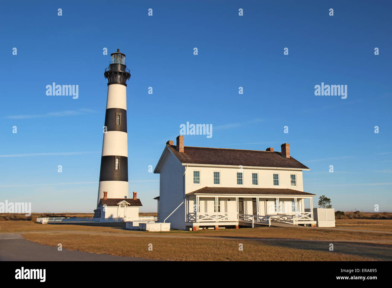The Bodie Island lighthouse and keeper's quarters at the Cape Hatteras National Seashore against a bright blue sky Stock Photo