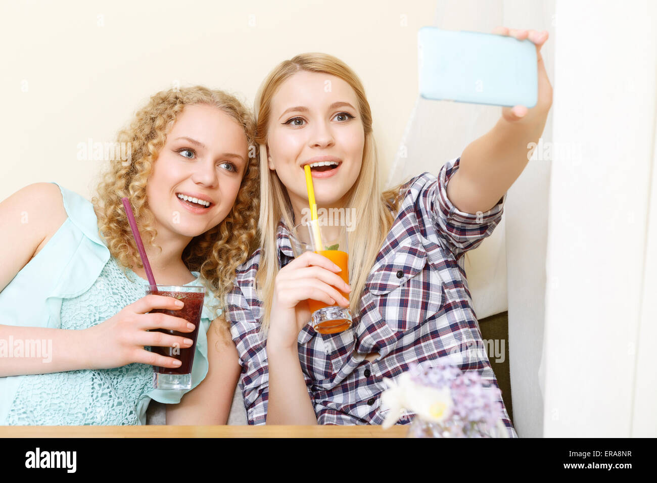 Two smiling girls doing selfie in cafe Stock Photo - Alamy