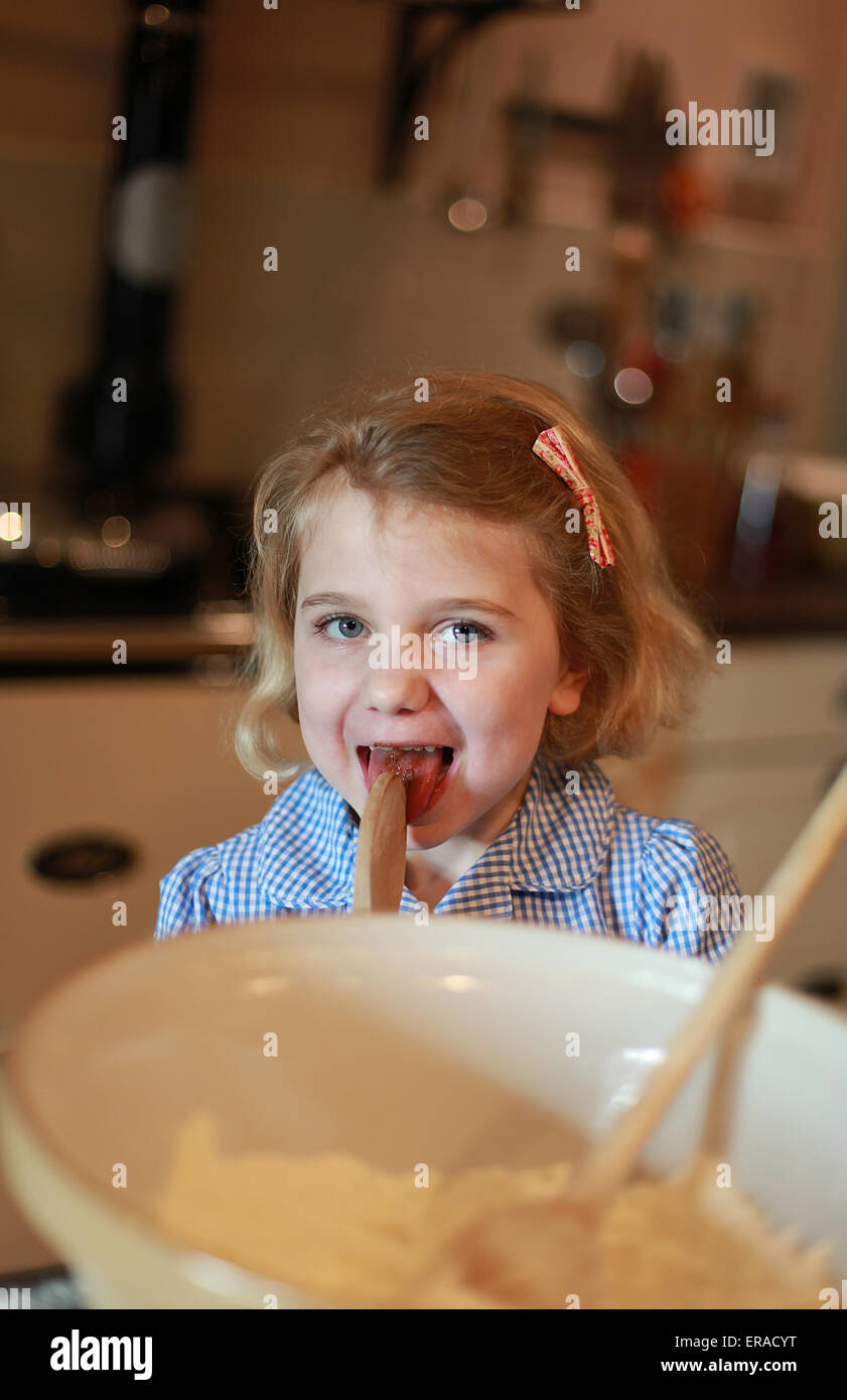 A young girl who has been baking is liking the spoon. Stock Photo