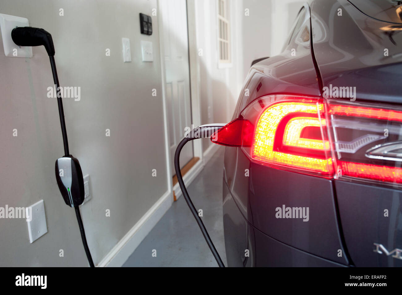 A Model S Tesla all electric car automobile being charged in a home garage Stock Photo