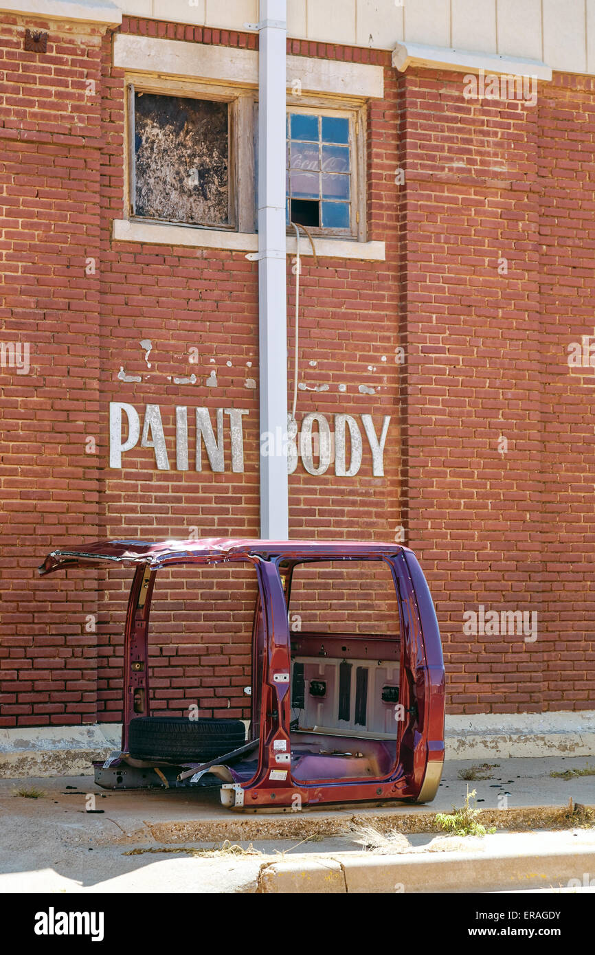 Paint & body shop letters on brick exterior of building.  Part of a truck body sits on the sidewalk under the sign. Stock Photo