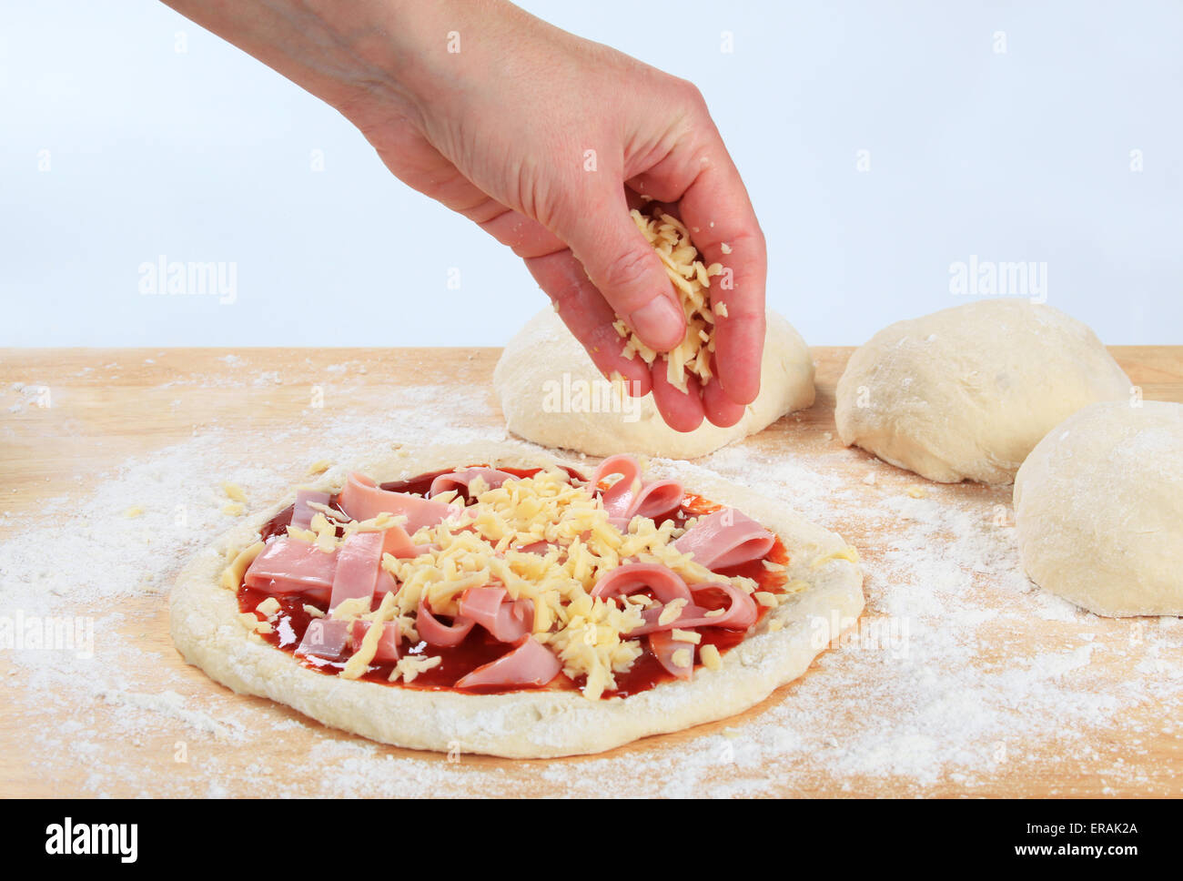Cook sprinkling shredded cheese over pizza Stock Photo Alamy