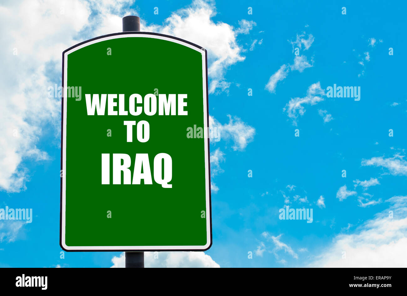 Green road sign with greeting message WELCOME TO IRAQ isolated over clear blue sky background with available copy space. Stock Photo