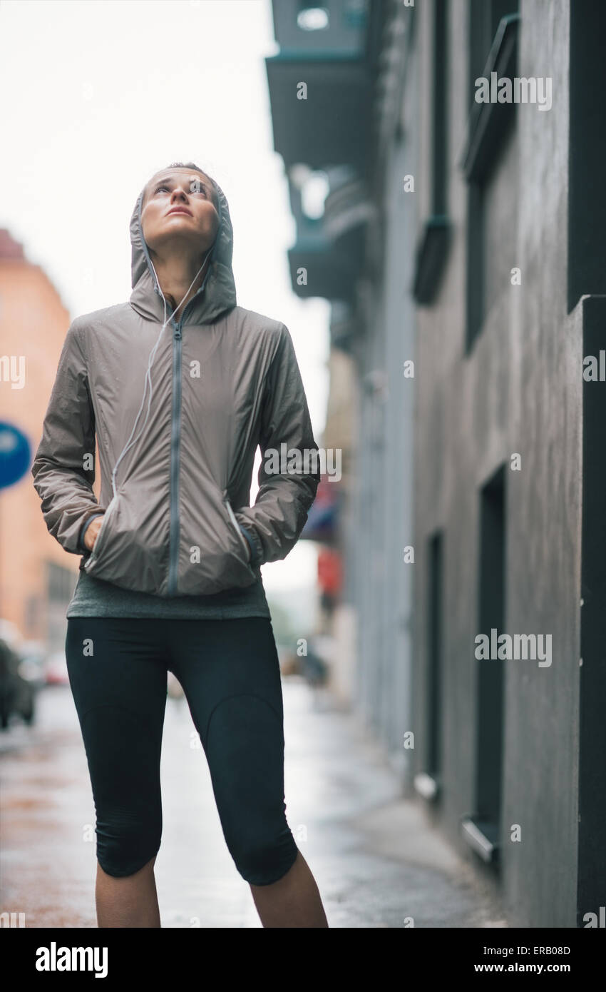 An athletic woman in workout and rain gear is looking up at the sky doubtfully, wondering if the rain will ever stop... Stock Photo