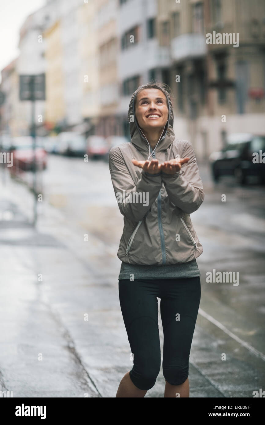 An athletic woman in workout and rain gear is looking up at the sky smiling holding her hands out playfully to catch some rain Stock Photo Alamy
