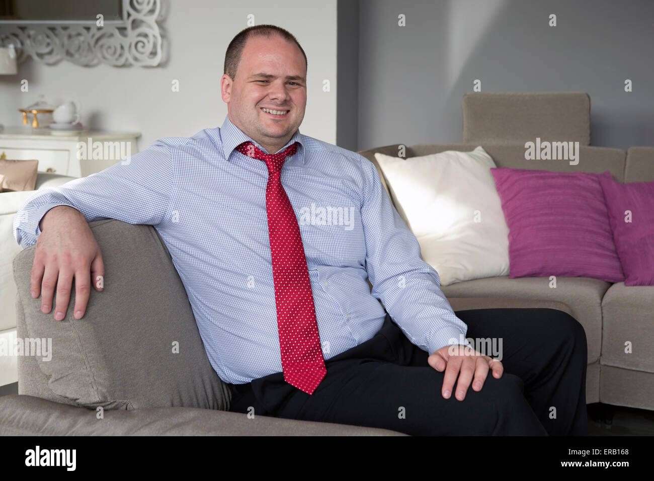 man in shirt and tie sits on couch and smiles Stock Photo