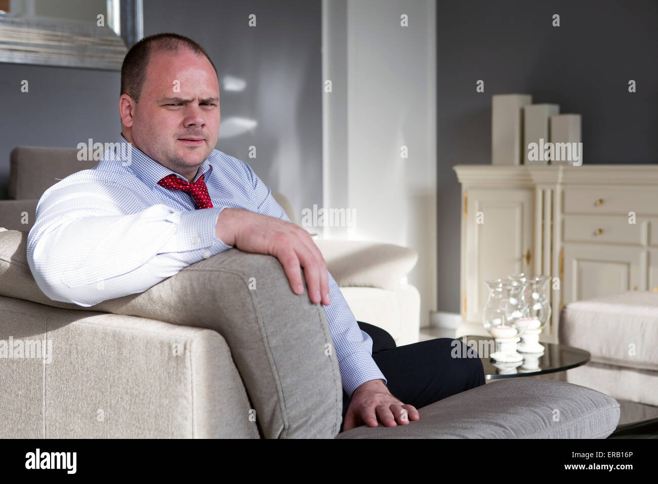 man in shirt and tie sits on couch and looks serious Stock Photo