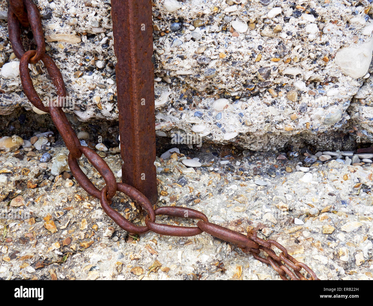 Rusting post and rusty and worn chain against a bettered concrete sea ...