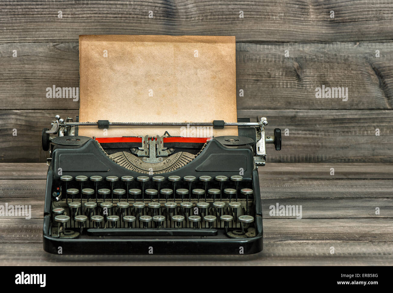 Antique typewriter with old textured paper page on wooden table. Vintage style toned picture Stock Photo